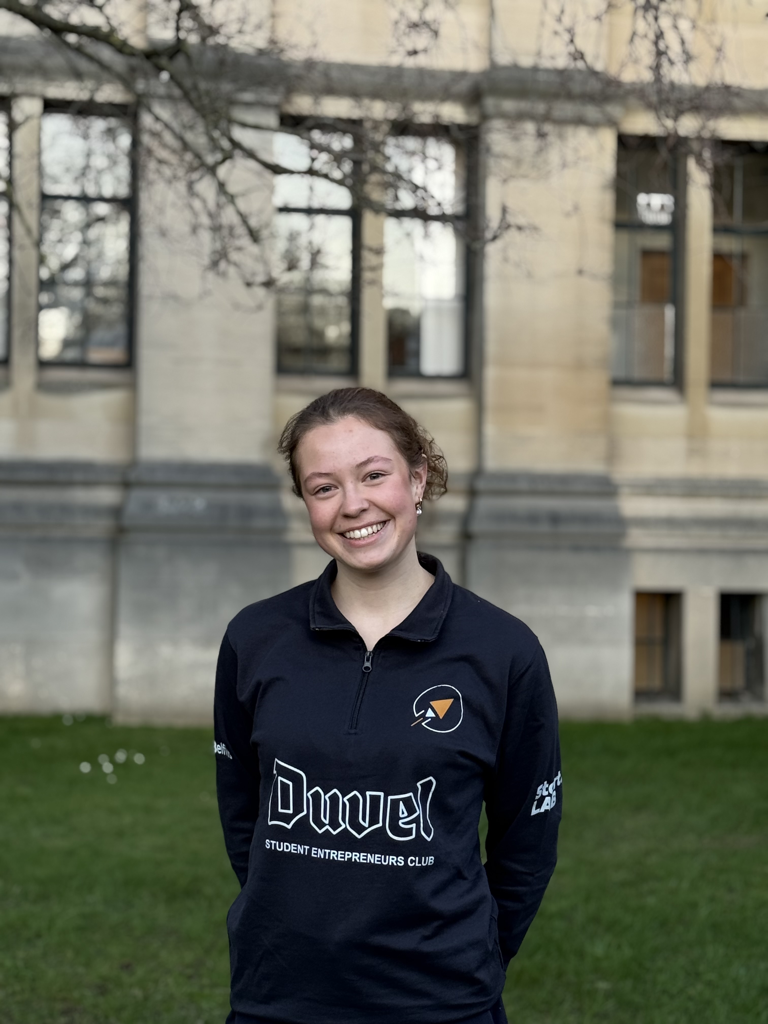 Portrait d'une jeune femme souriante aux cheveux blonds attachés, portant une veste noire.