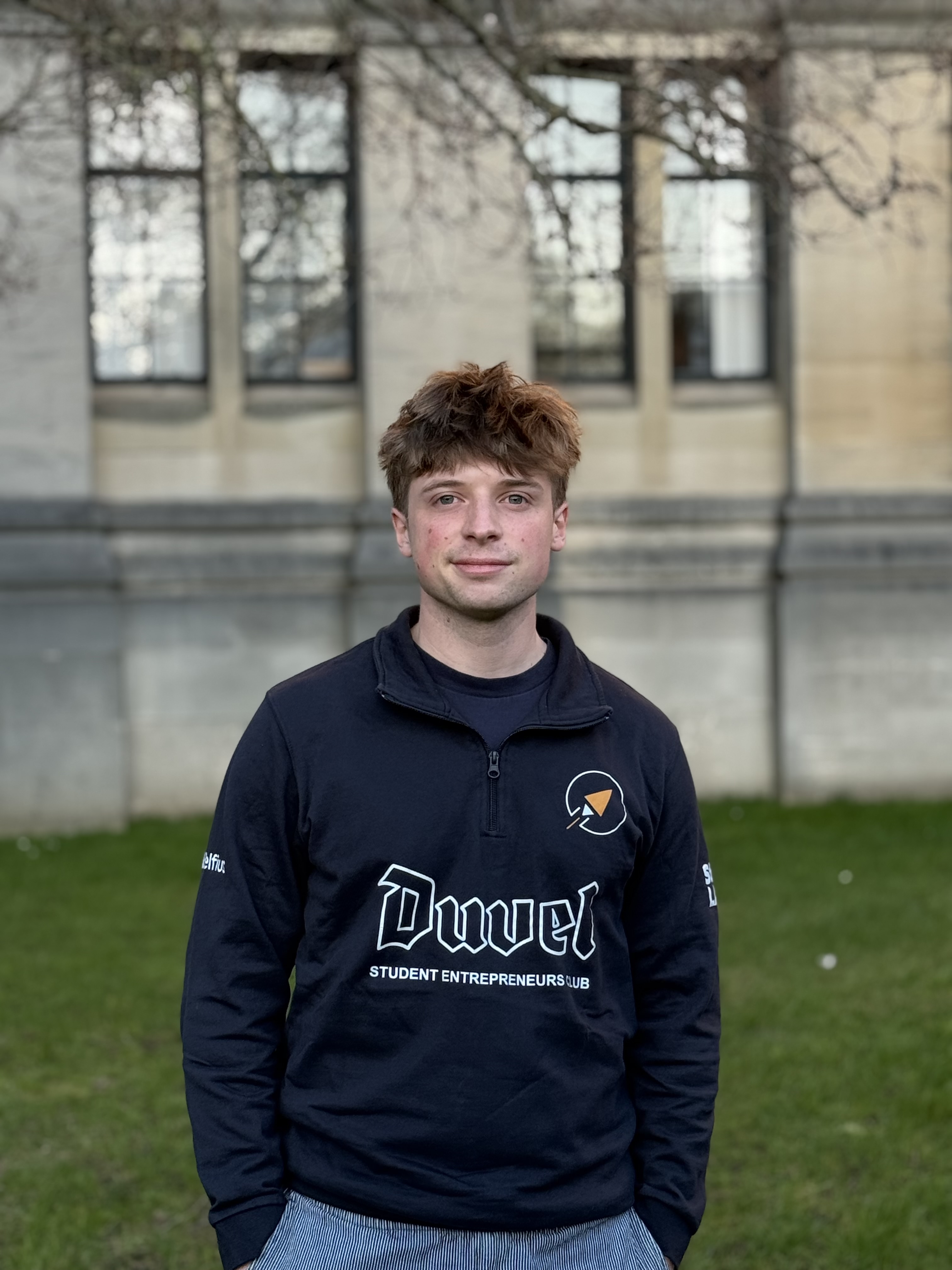 Portrait d'un jeune homme aux cheveux blonds ébouriffés portant une veste noire, fond flou clair.