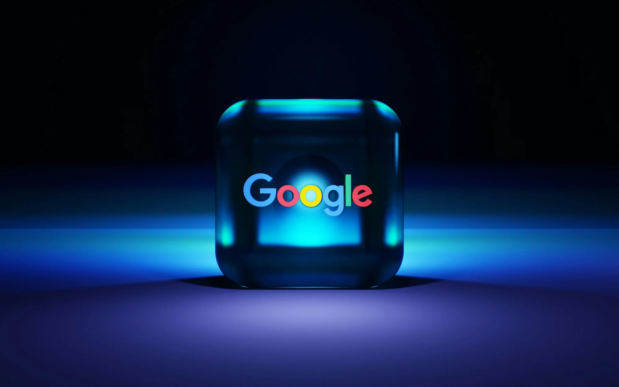 Illuminated translucent cube with the colorful Google logo at its center on a dark blue lit surface.
