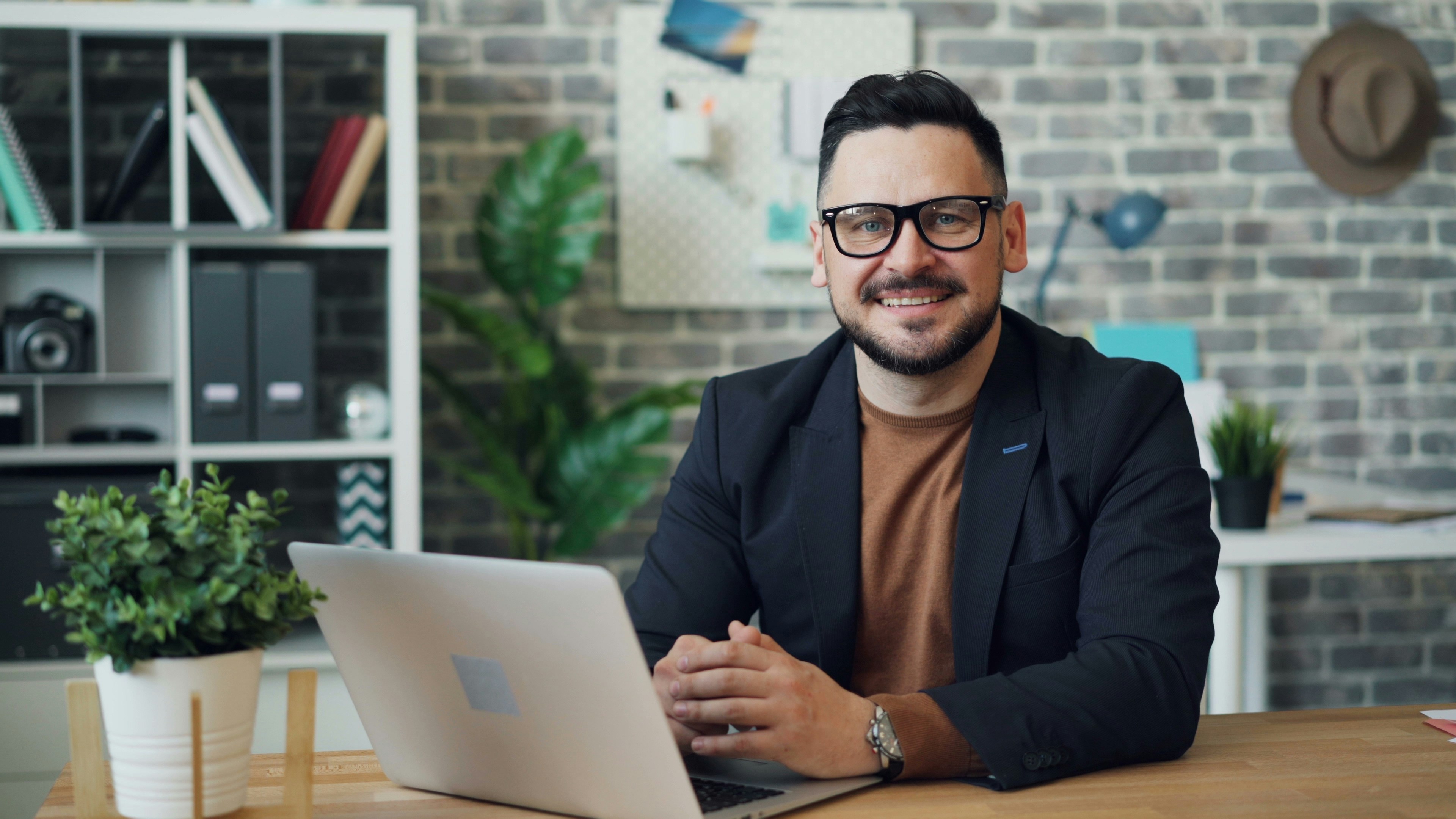 Mid-career professional male sitting at desk with laptop computer smiling at camera