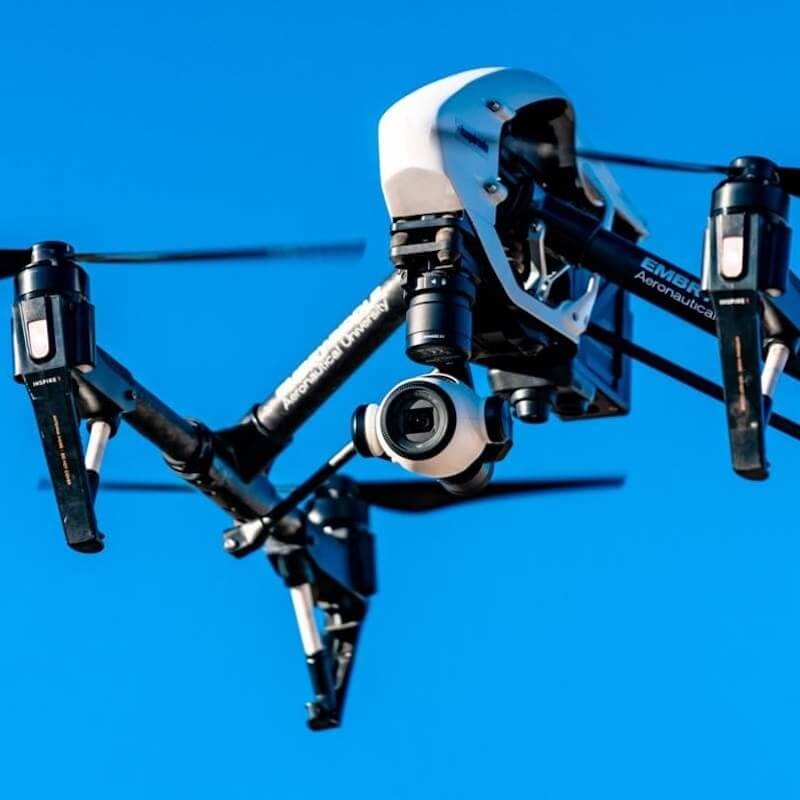 Close-up of a black and white camera drone flying against a clear blue sky.