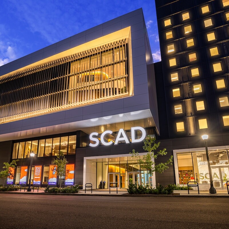 Evening view of a modern SCAD building with illuminated signage and large windows.