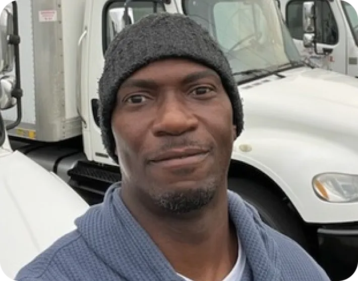 Man wearing a gray knit beanie and blue sweater standing outside near white trucks.