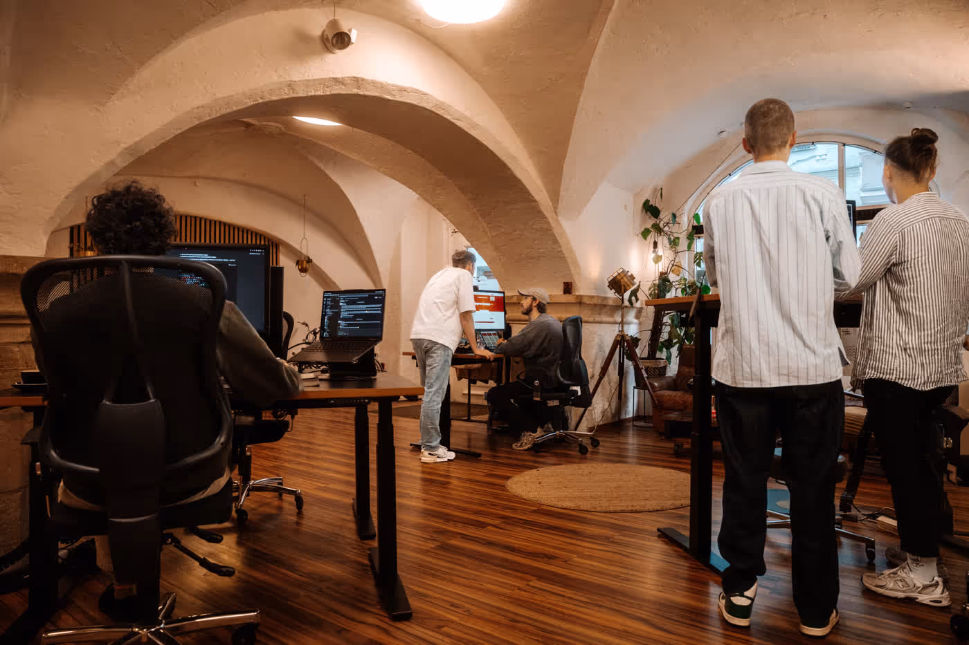 Ein Büro mit gewölbtem Decken und fünf Personen, die an Computern arbeiten und zusammenarbeiten.