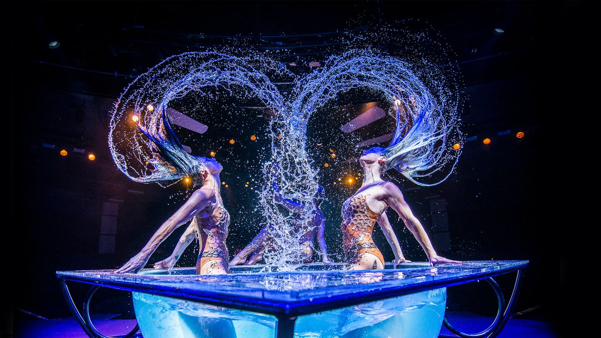 Two WOW performers whipping their hair in arcs of water over a glass tank