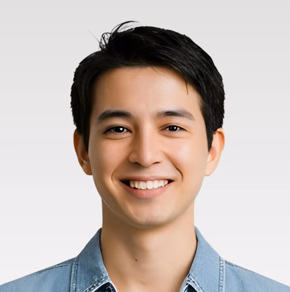Smiling young man with short black hair wearing a blue denim shirt against a light background.