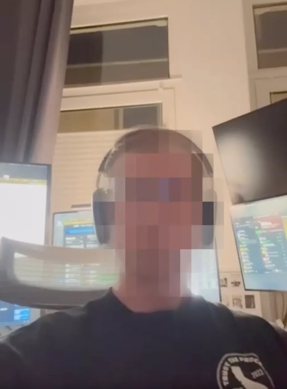 Person wearing headphones seated in front of multiple computer monitors in a room with tall windows and a curtain.