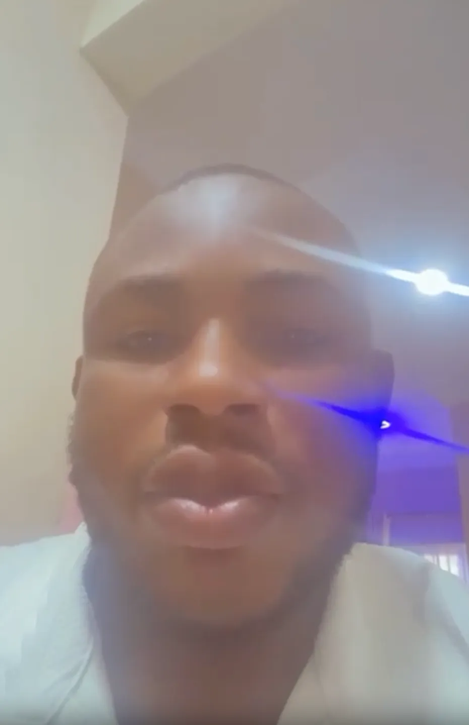 Close-up of a man's face with short hair and beard indoors, light glare partially obscuring his features.