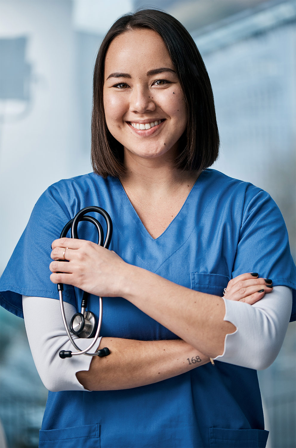 Smiling nurse in blue scrubs with folded arms holding a stethoscope.