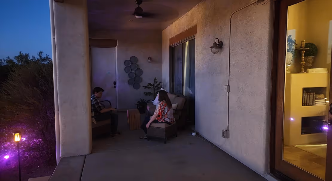 Two people sitting on a covered patio at dusk, talking in soft ambient lighting.
