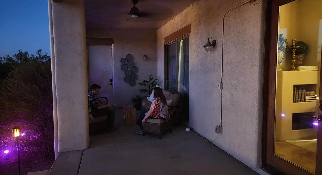 Two people sitting on a covered patio at dusk, talking in soft ambient lighting.