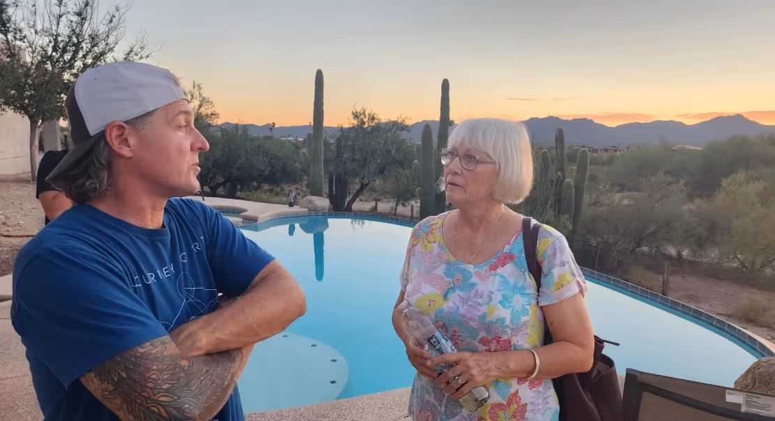 Two adults having a conversation near a pool at sunset with desert scenery behind them.