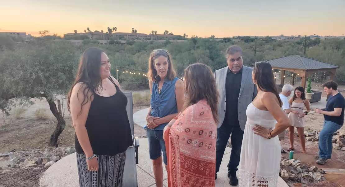 Several people standing and talking outdoors at sunset with desert plants and a gazebo in the background.