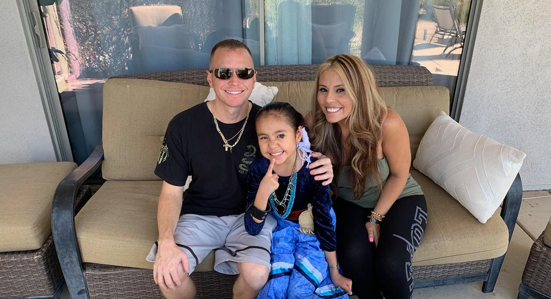 Two adults and a child sitting together on an outdoor couch and smiling.