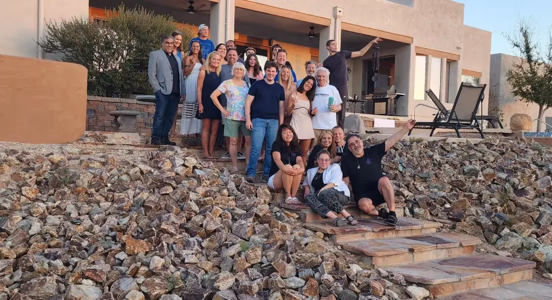 Large group of people posing for a photo on stone steps outside a house at sunset.