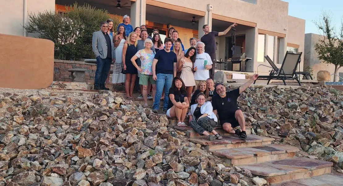 Large group of people posing for a photo on stone steps outside a house at sunset.