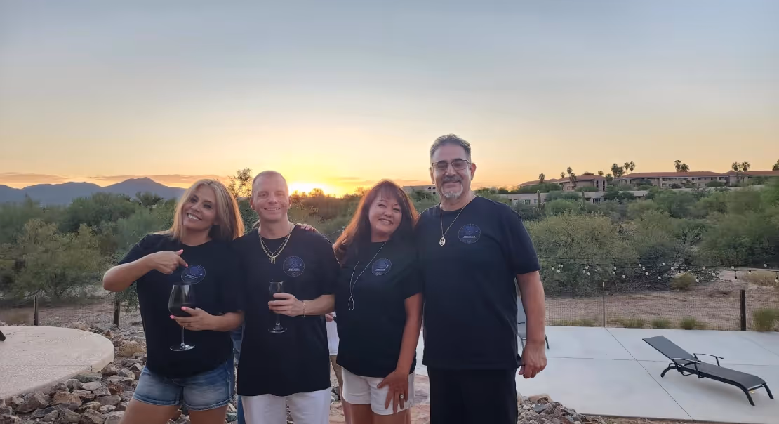 Four adults standing together outdoors at sunset, posing and smiling.