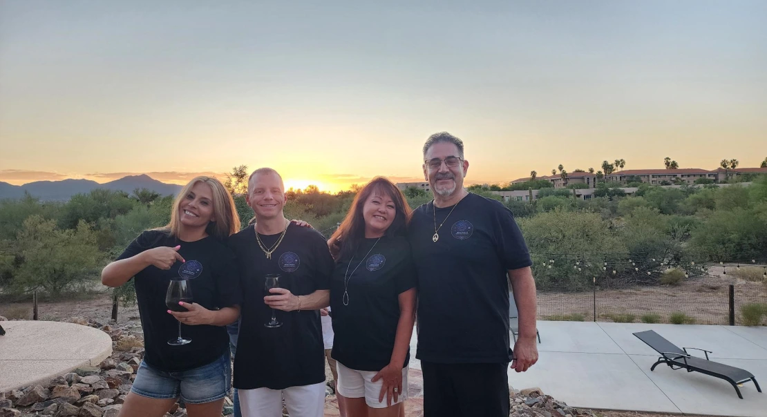 Four adults standing together outdoors at sunset, posing and smiling.
