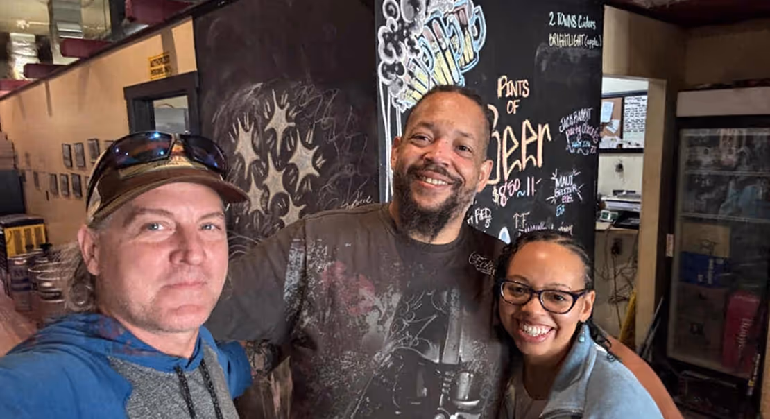 Mike Grady and two retreat attendees smiling and posing for a photo inside a casual café with chalkboard art behind them.