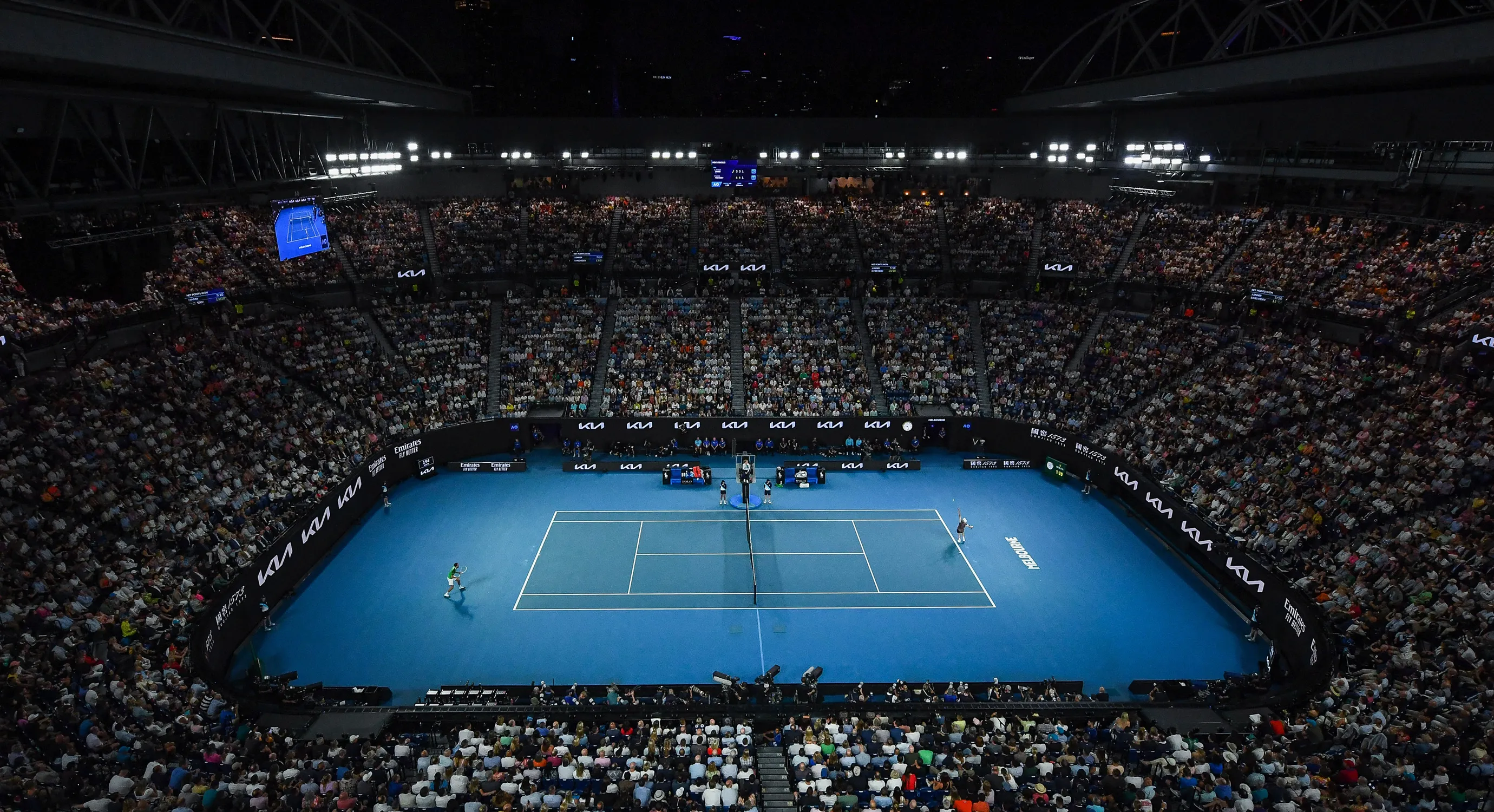 Crowded stadium with audience watching a professional tennis match on a blue court.