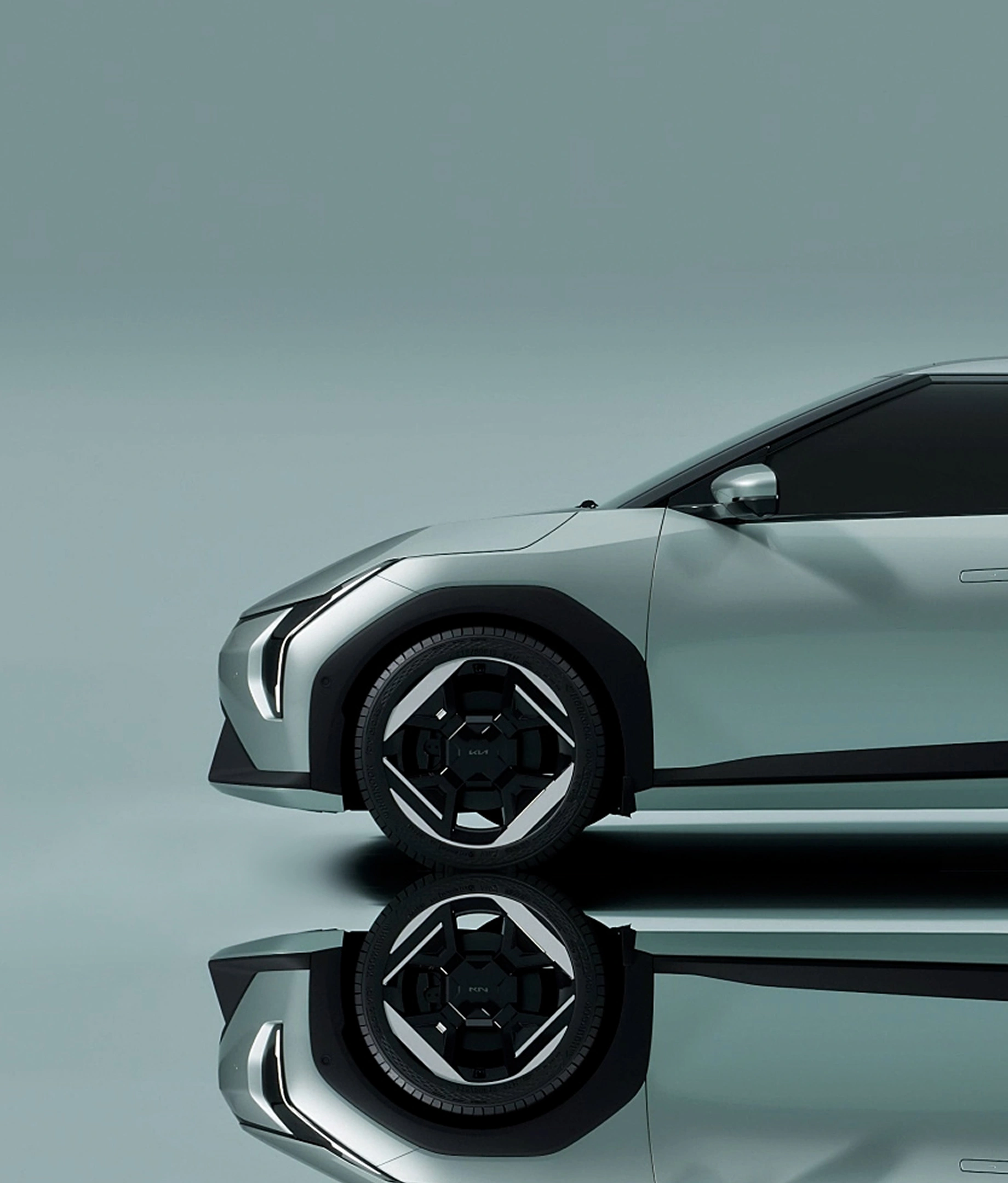 Side view of a silver modern electric car front half with sleek design and black wheel, reflected on glossy surface.