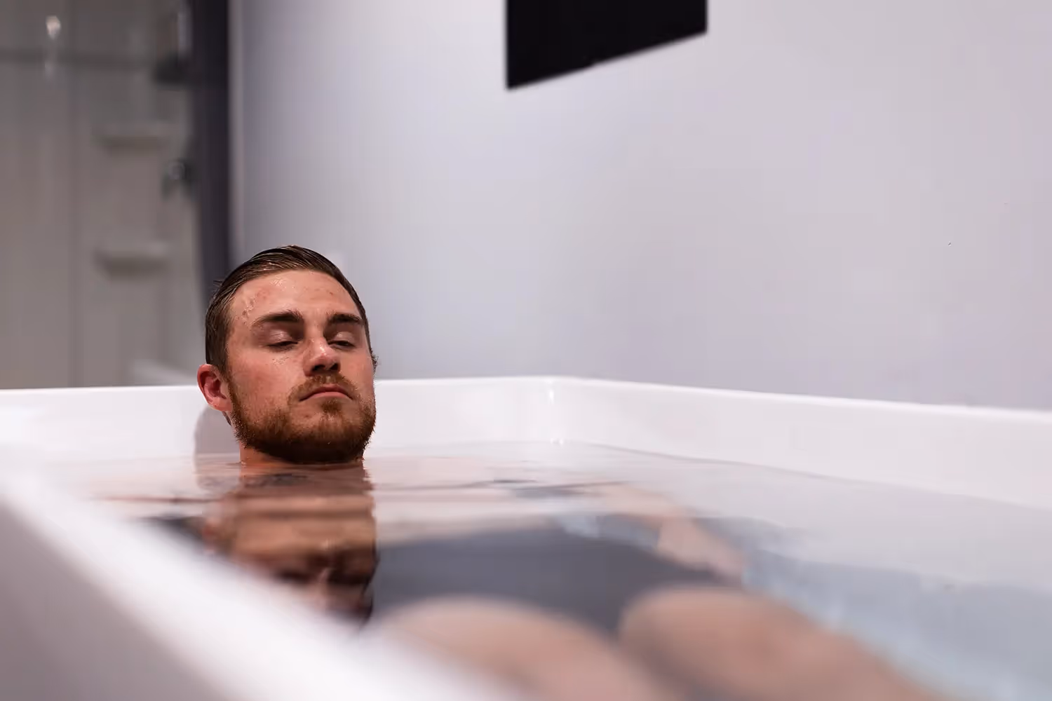 Man with closed eyes relaxing in a bathtub filled with water.