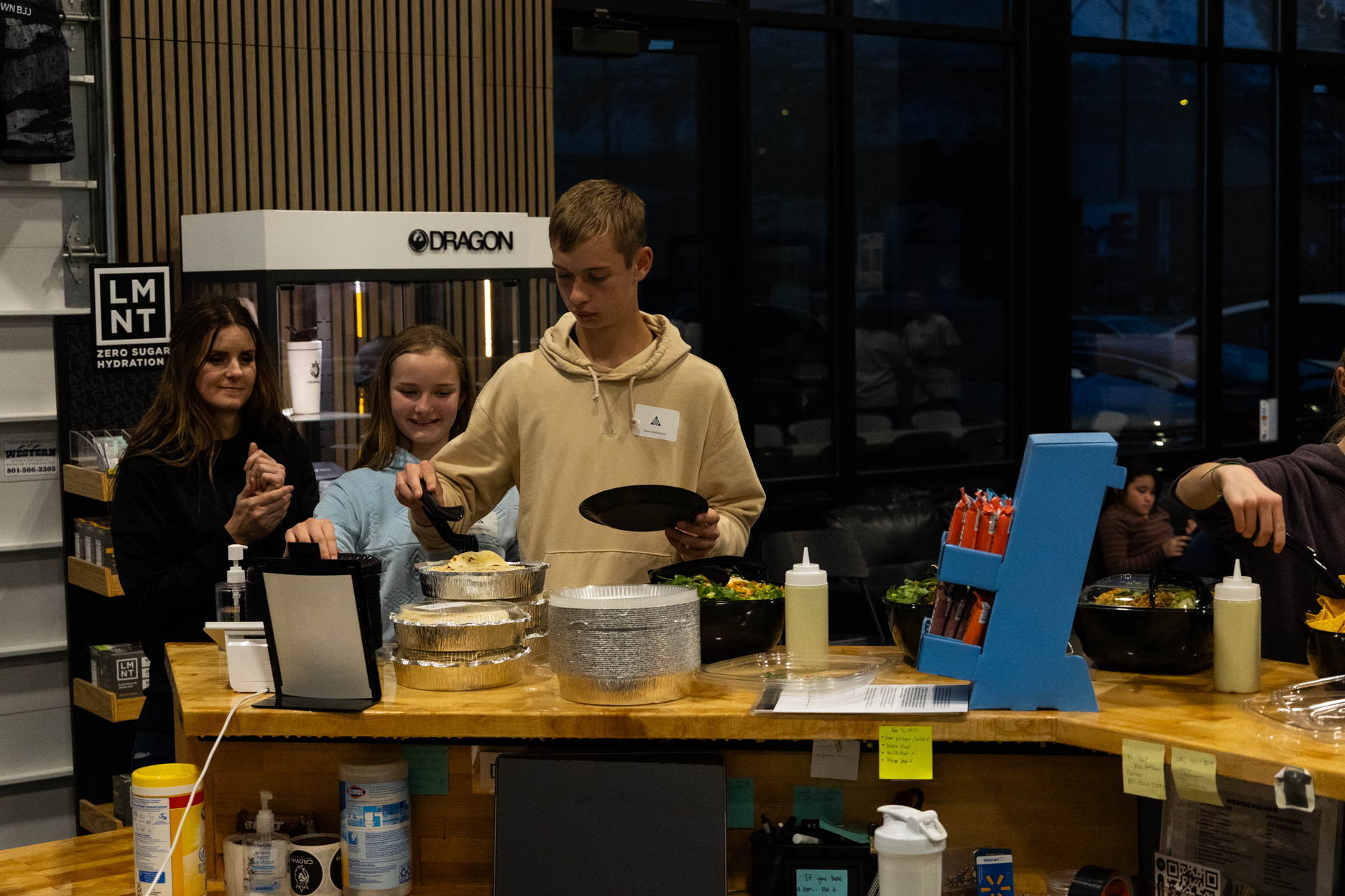 People serving themselves food from containers on a wooden counter in a casual indoor setting.