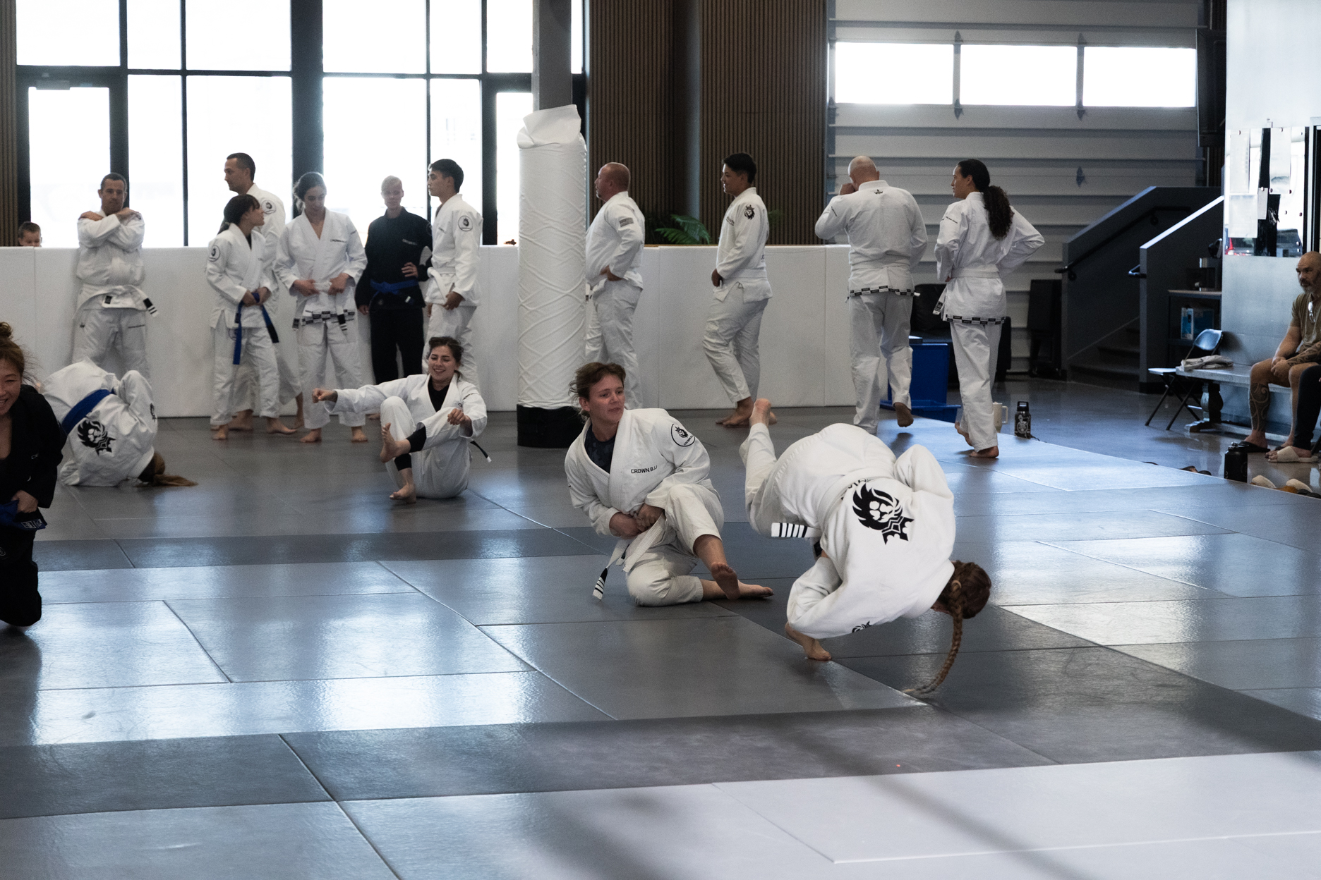 People practicing Brazilian Jiu-Jitsu in white and blue gis inside a martial arts gym.