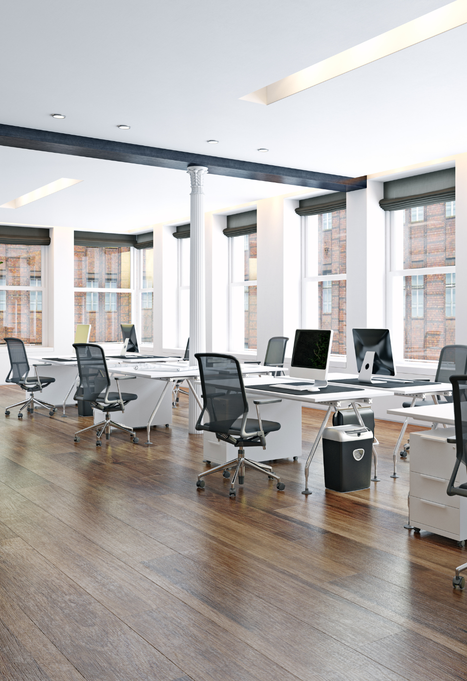 Modern open-plan office with multiple white desks, black mesh chairs, desktop computers, large windows, and wooden flooring.