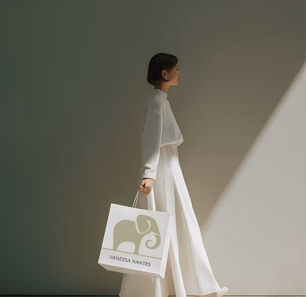 Woman in white outfit walking and holding a shopping bag with a beige elephant logo and the text Vanessa Nantes.