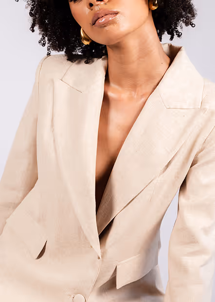 Close-up of a woman wearing a beige blazer with gold hoop earrings and natural curly hair.