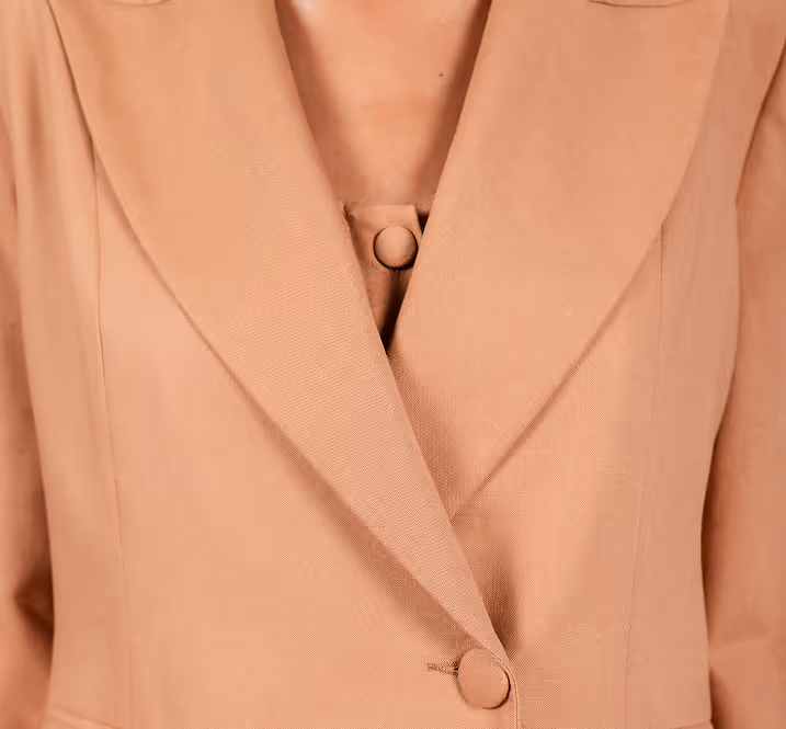 Close-up of a person wearing a light brown blazer with a matching buttoned top underneath.