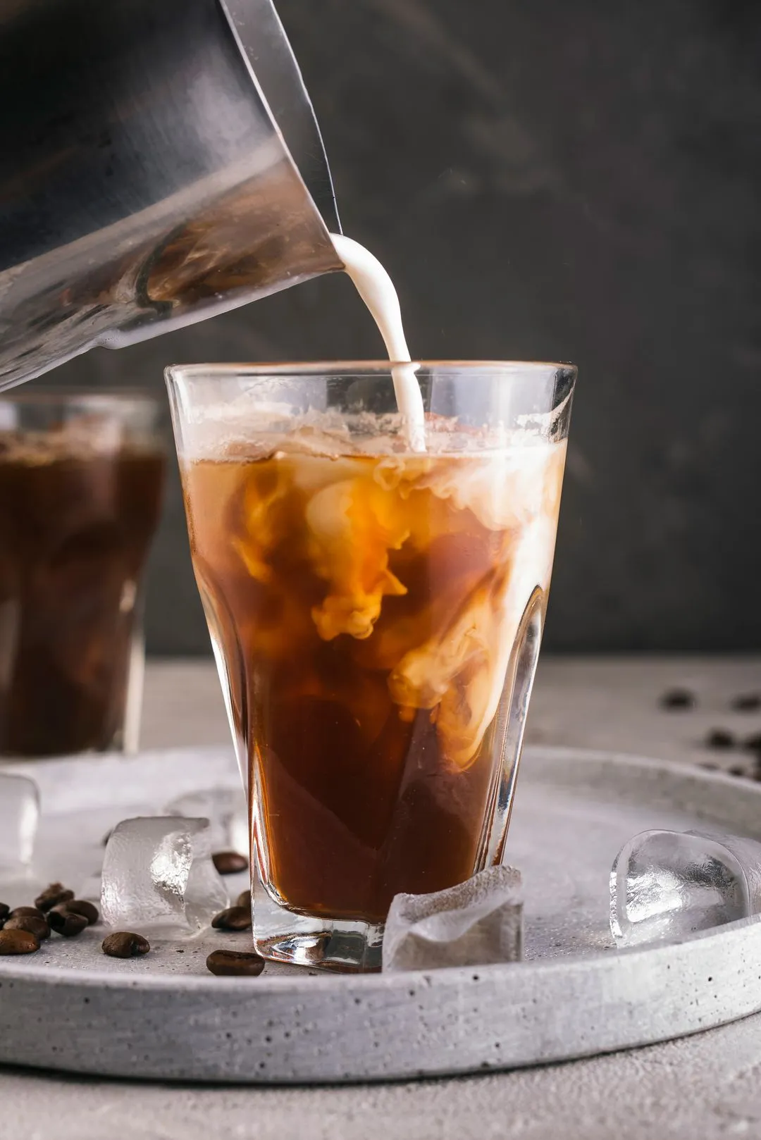 Milk swirling into iced coffee in glass