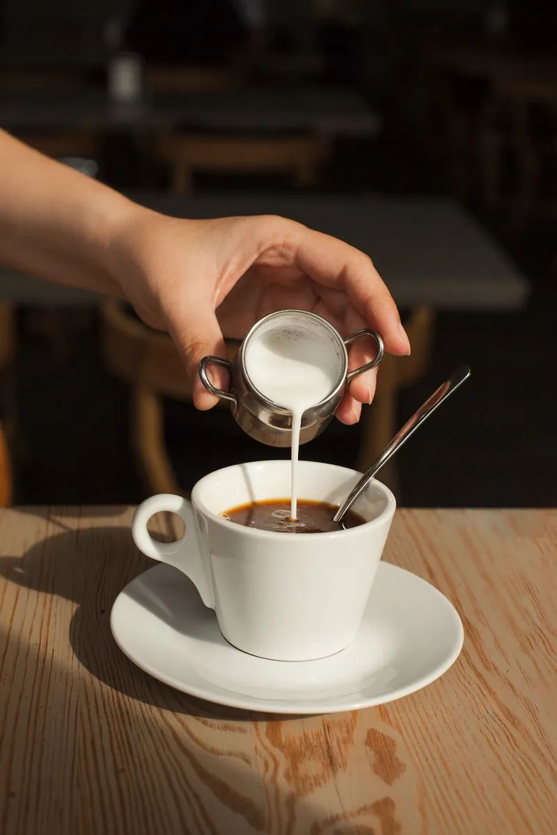 Milk being poured into black coffee in white cup