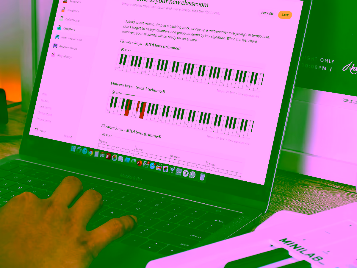 Person using a MacBook Pro displaying a music lesson interface with piano keys and music notation, next to a MINILAB keyboard controller.