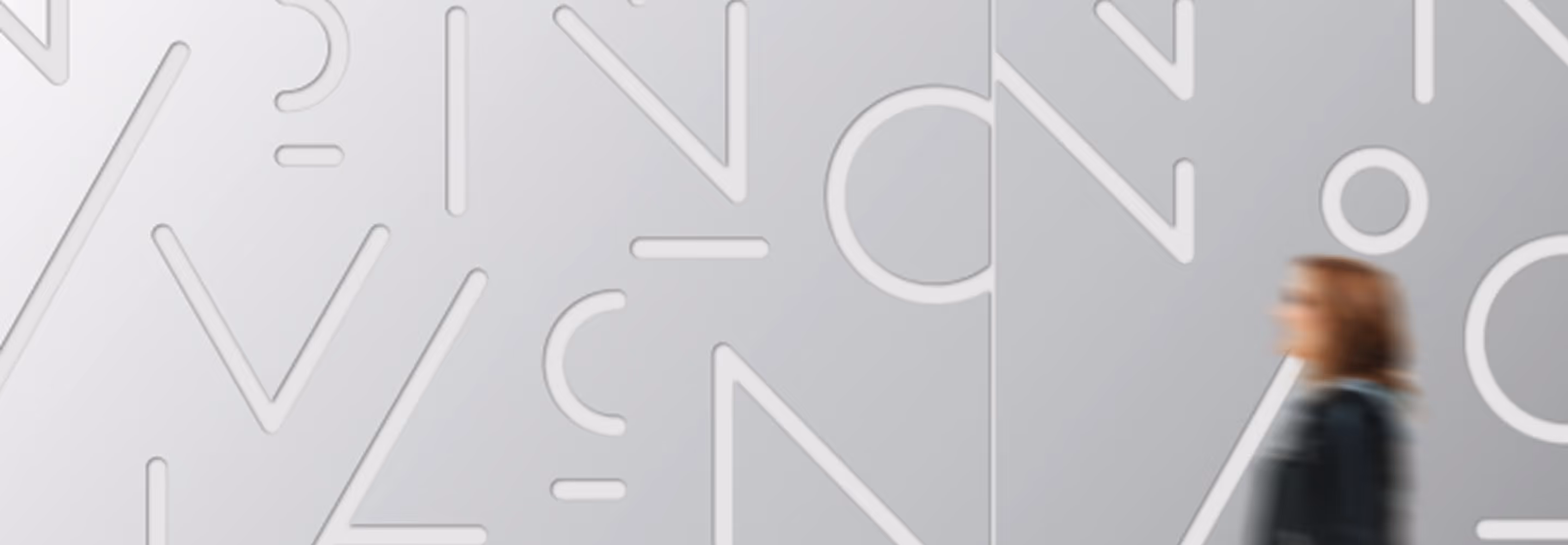 Phot of Metal wall with abstract letter shapes and a blurry wman in the corner contributing a sense of movement