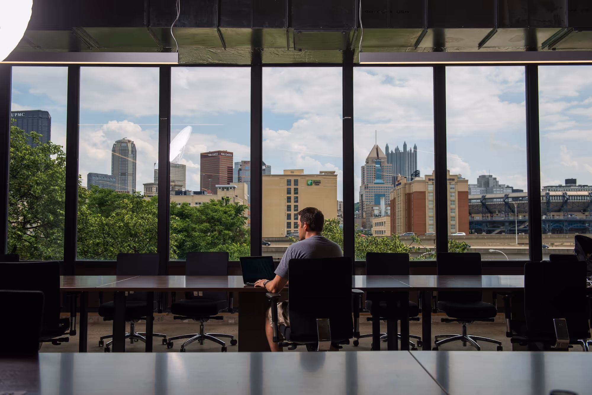 Image of man sitting in a conference room alone in front of large windows overlooking Pittsburgh.