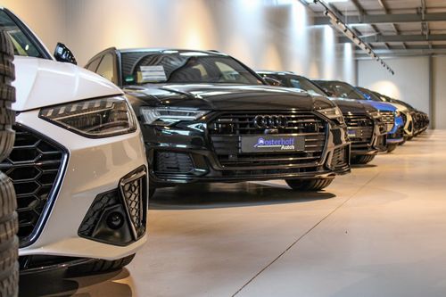 Line of parked Audi cars in an indoor showroom with polished floor and ceiling lights.