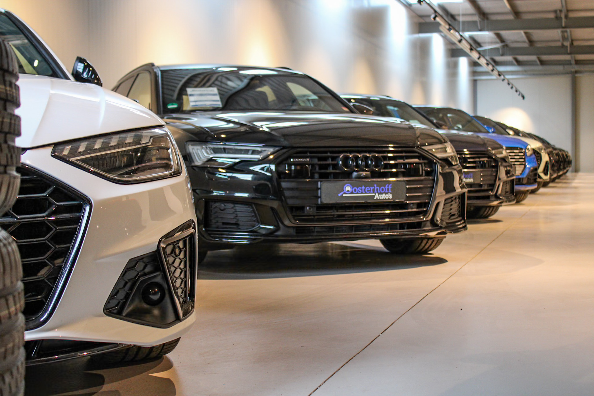Line of parked Audi cars in an indoor showroom with polished floor and ceiling lights.