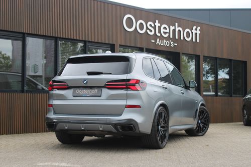 Rear view of a matte silver BMW SUV parked outside Oosterhoff Auto's dealership.