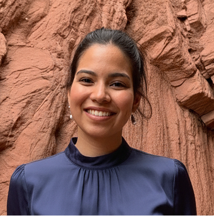 Smiling woman with dark hair in a navy blue blouse standing in front of textured reddish rock formations.