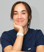 Smiling woman with dark hair resting her chin on her hand wearing a navy blue top and white smartwatch.