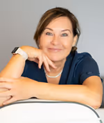 Smiling woman with short hair resting her chin on her hand against a plain light gray background.