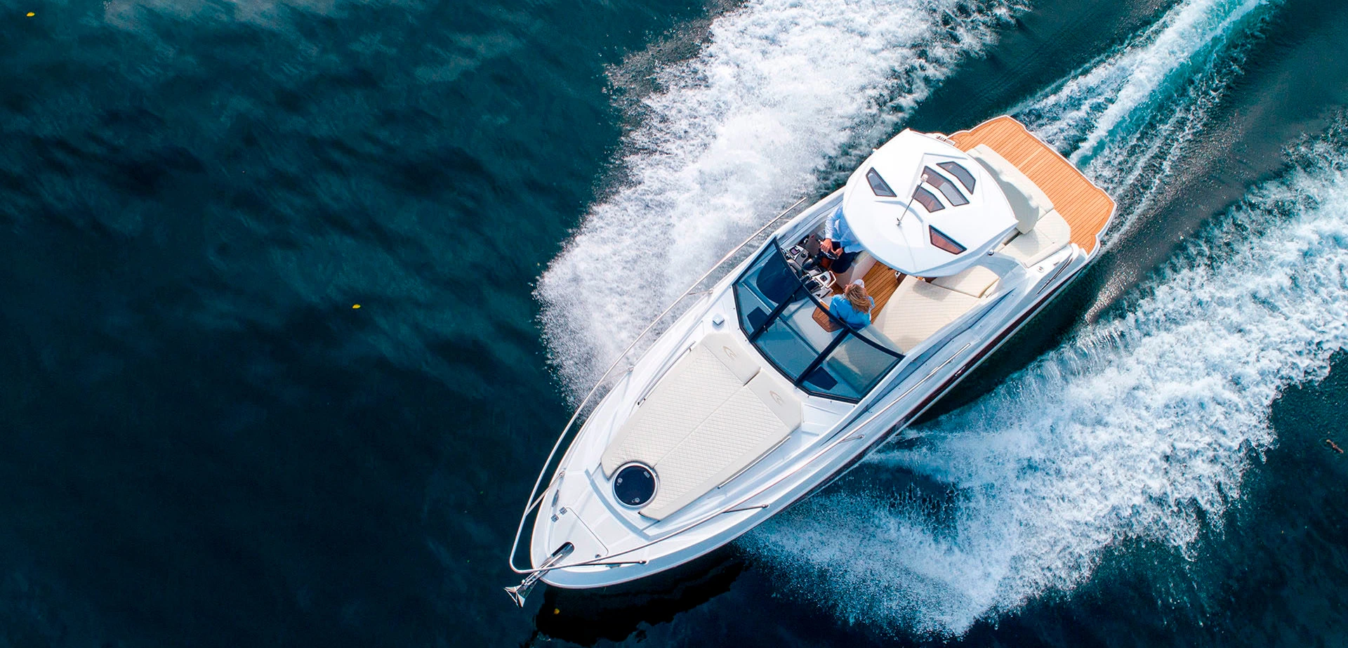 A white motorboat cruising swiftly on deep blue water with two people seated inside.