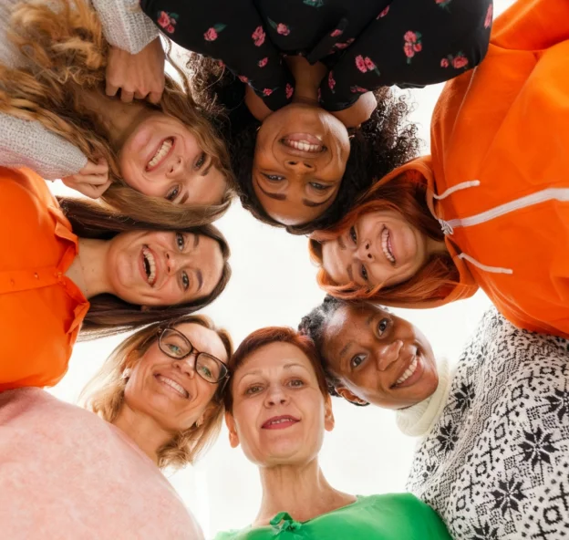 Group of diverse women standing in a circle looking down and smiling at the camera.