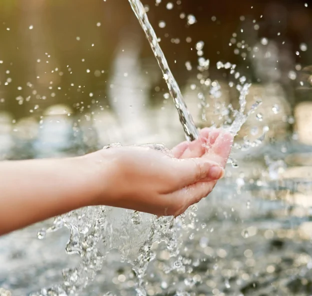 Close-up of a hand catching a stream of flowing water with splashes around.