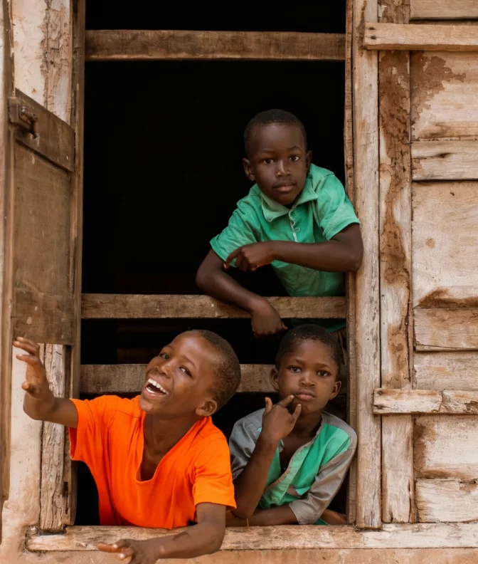 Three boys looking out and leaning through a wooden window frame, one smiling and reaching out.
