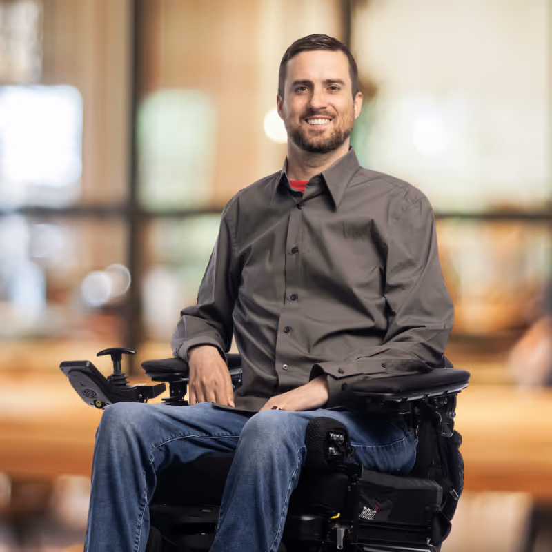 Tyson Gentry wearing a gray button-up shirt and blue jeans with a blurred indoor background.