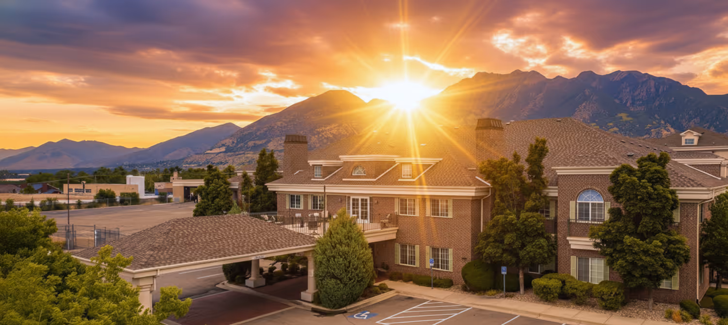 Sunset over a brick residential building with a covered driveway and mountains in the background.