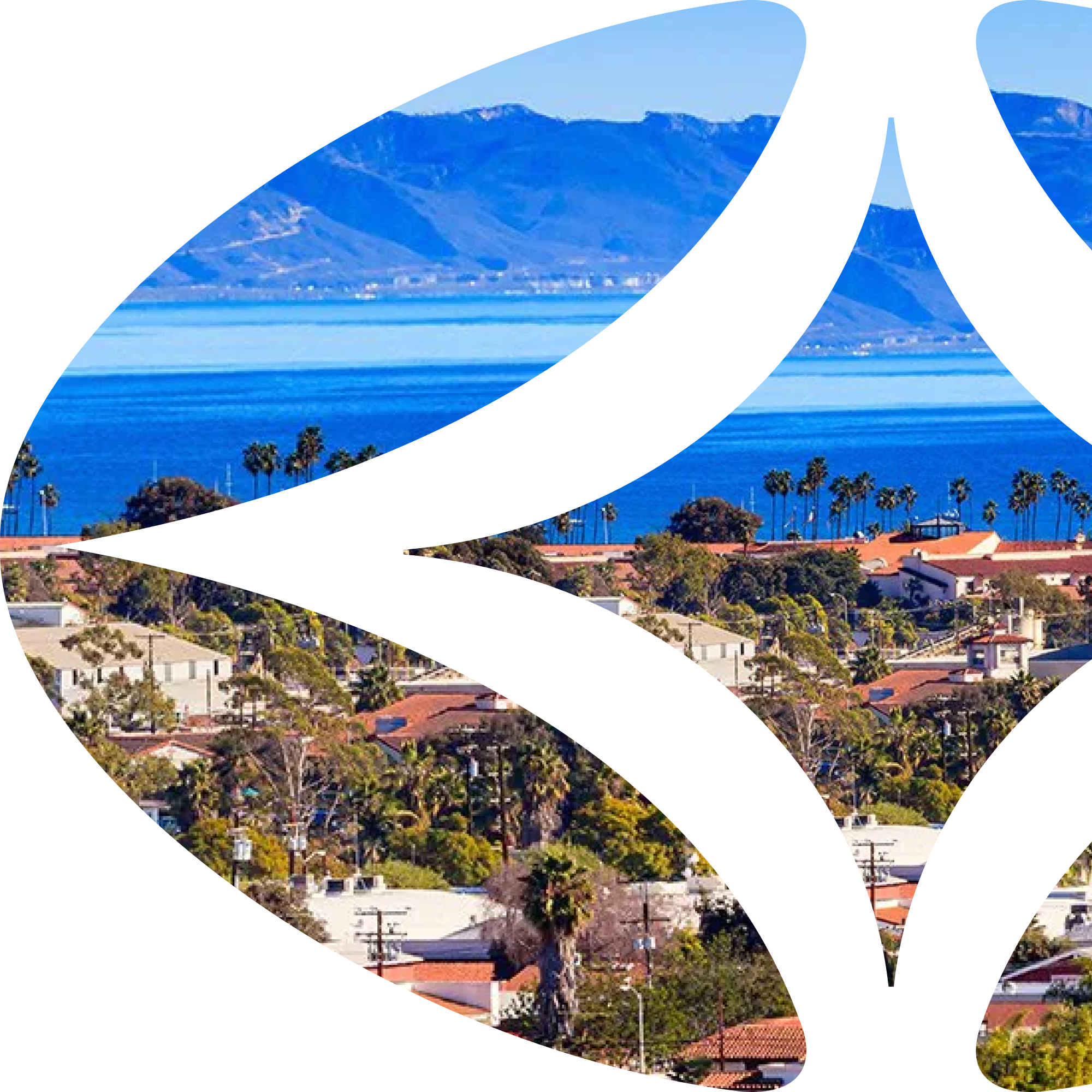 Coastal cityscape with red-tiled roofs, palm trees, and mountains across a blue ocean under a clear sky.